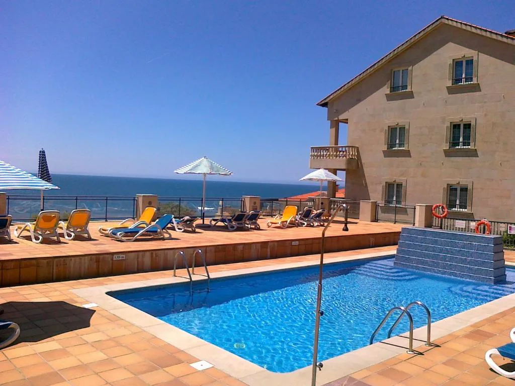 Piscina exterior con tumbonas y vistas al mar junto al edificio del hotel, Talaso Atlántico
