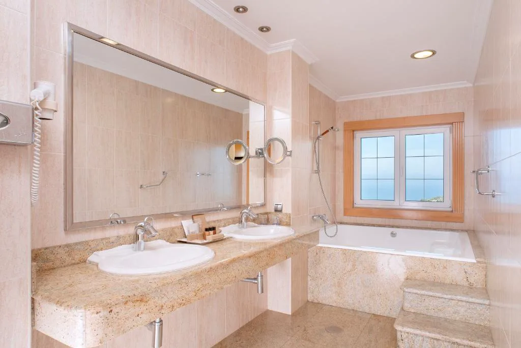 Baño en tonos crema con bañera, doble lavabo y ventana con vistas al mar, Talaso Atlántico