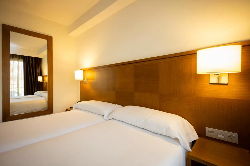Habitación doble con cabecero de madera e iluminación cálida, Hotel Thalasso Cantabrico Las Sirenas