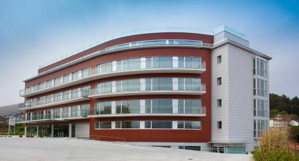 Fachada curva del Hotel Thalasso Cantabrico Las Sirenas sobre la ladera junto a la playa de Sacido, Viveiro