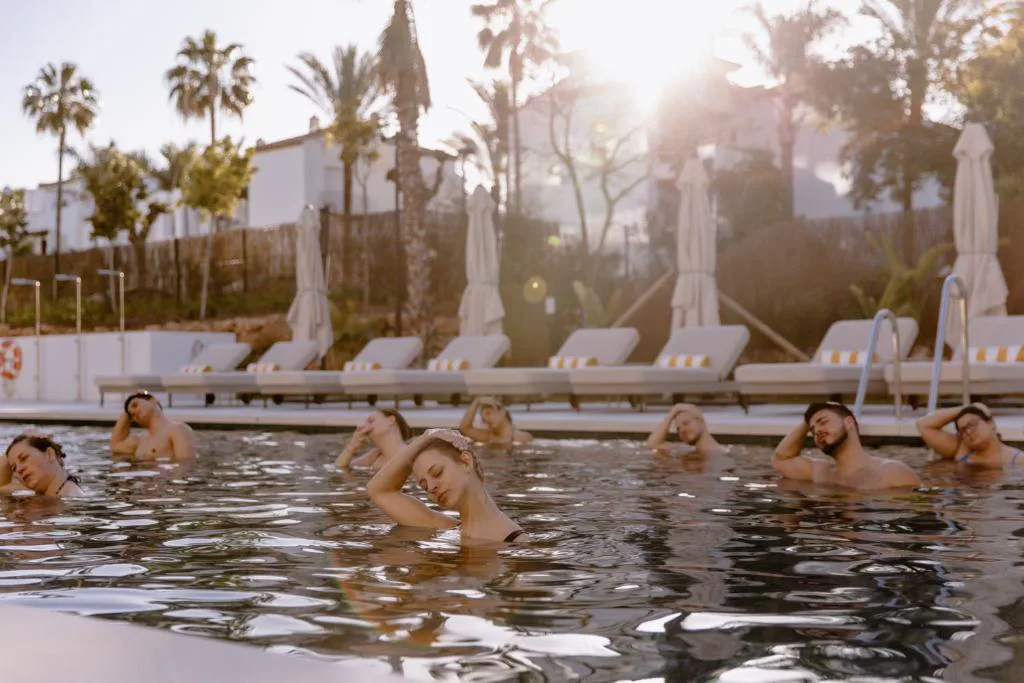 Personas en la piscina con tumbonas al fondo