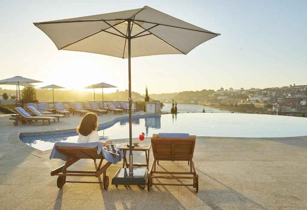 Pareja relajándose junto a la piscina infinita al atardecer, con Oporto al fondo, The Yeatman