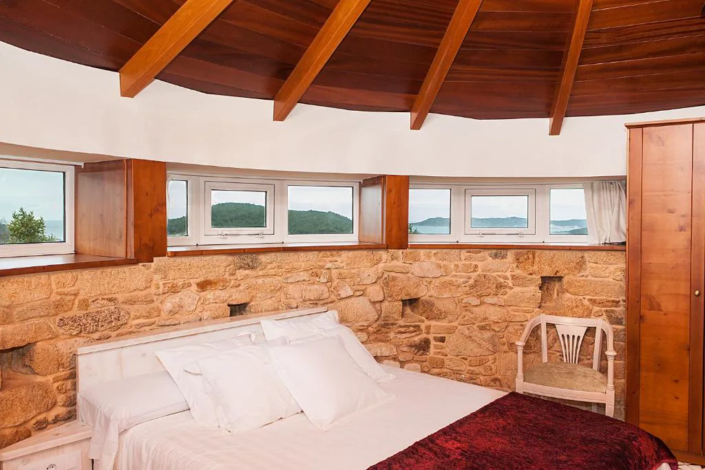 Dormitorio circular de piedra con vistas panorámicas al mar a través de ventanas curvas, A Torre de Laxe