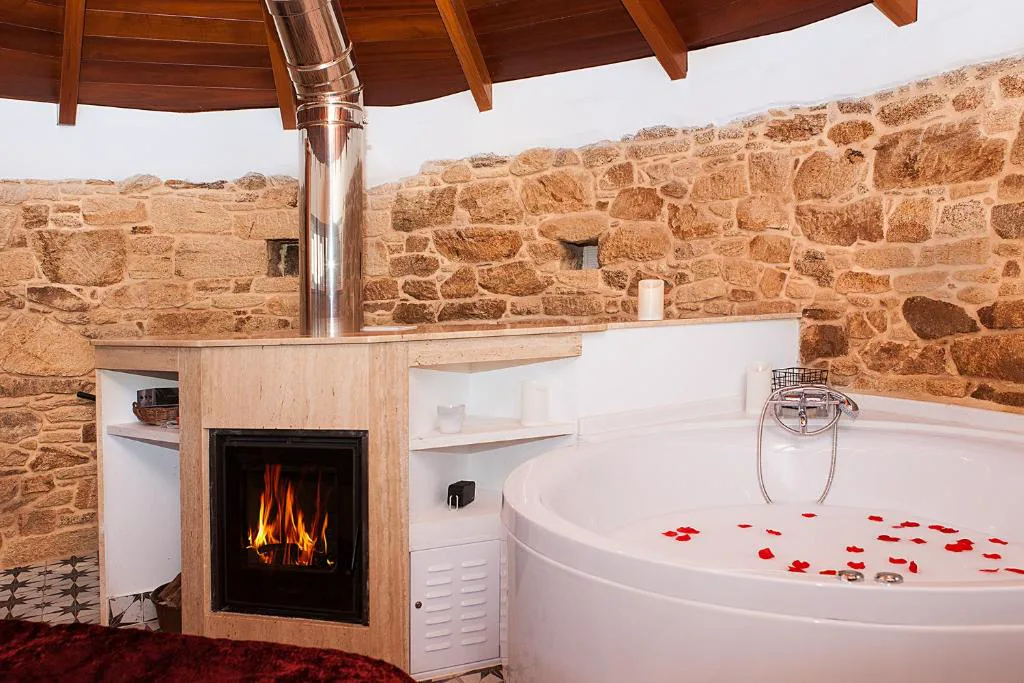 Bañera de hidromasaje junto a chimenea de leña encendida en habitación circular de piedra, A Torre de Laxe