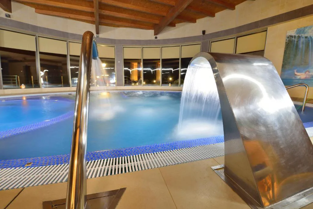Cascada de acero sobre la piscina de hidromasaje iluminada de noche, Hotel Spa Norat Torre do Deza