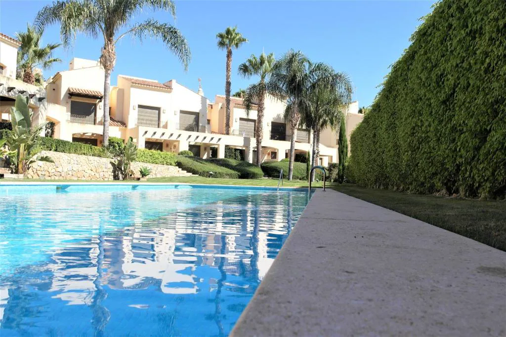 Piscina comunitaria con casas adosadas y palmeras junto al jardín