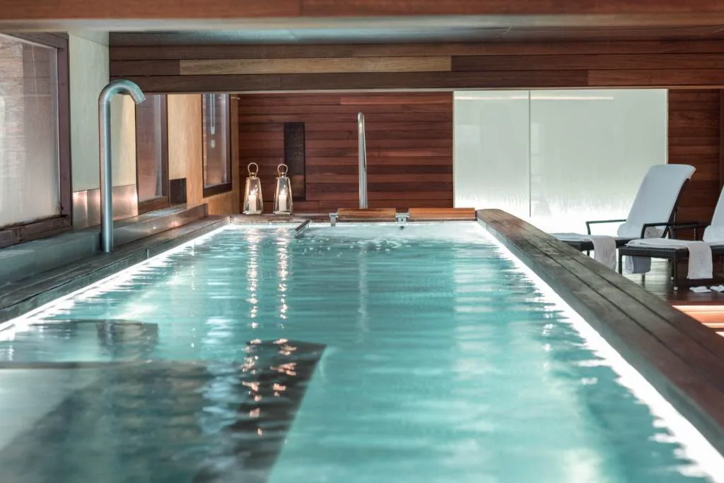 Piscina interior del spa con carril de agua, iluminación cálida y tumbonas