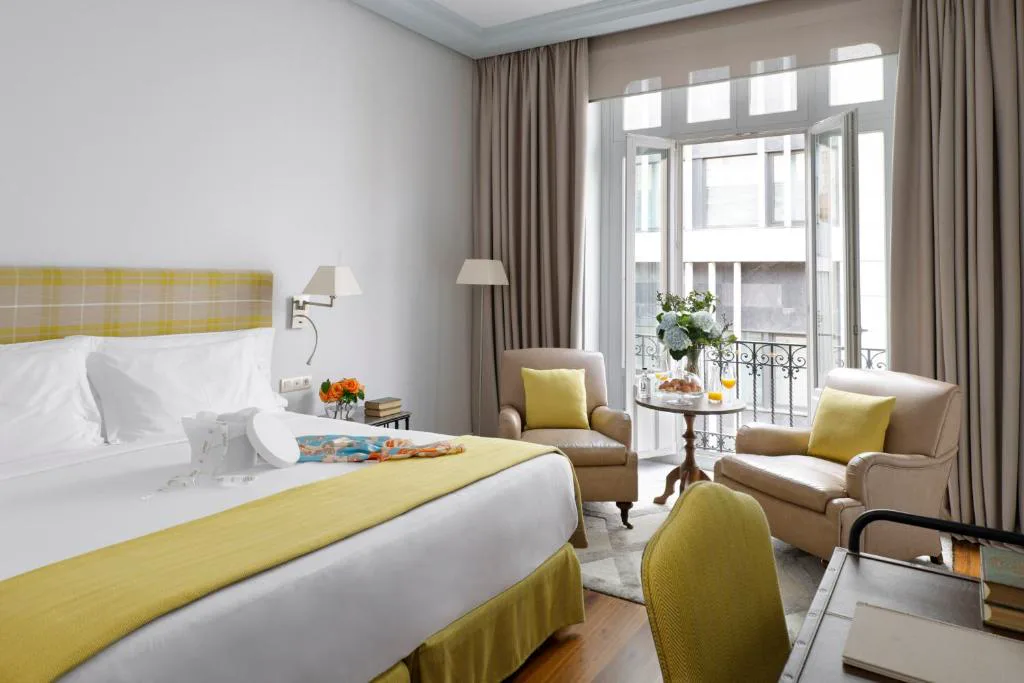 Habitación con cabecero amarillo, sillones y balcón a la calle
