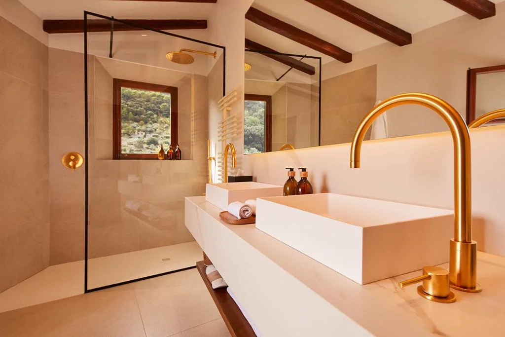 Baño con ducha acristalada, grifería dorada y vistas al valle, Valldemossa Hotel