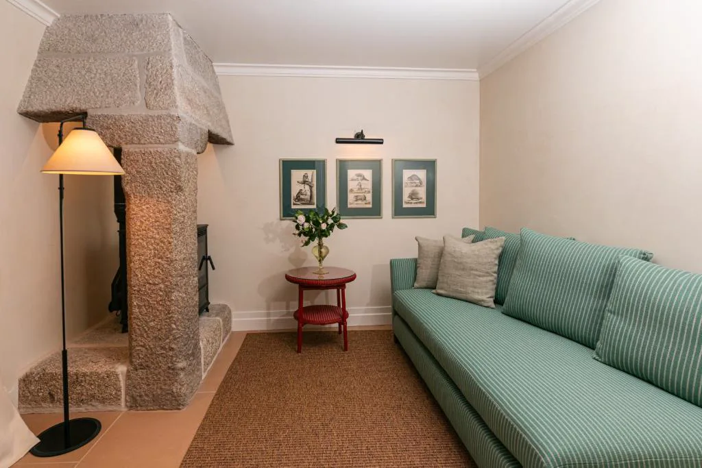 Salón con chimenea de granito original y sofá verde, Valverde Santar