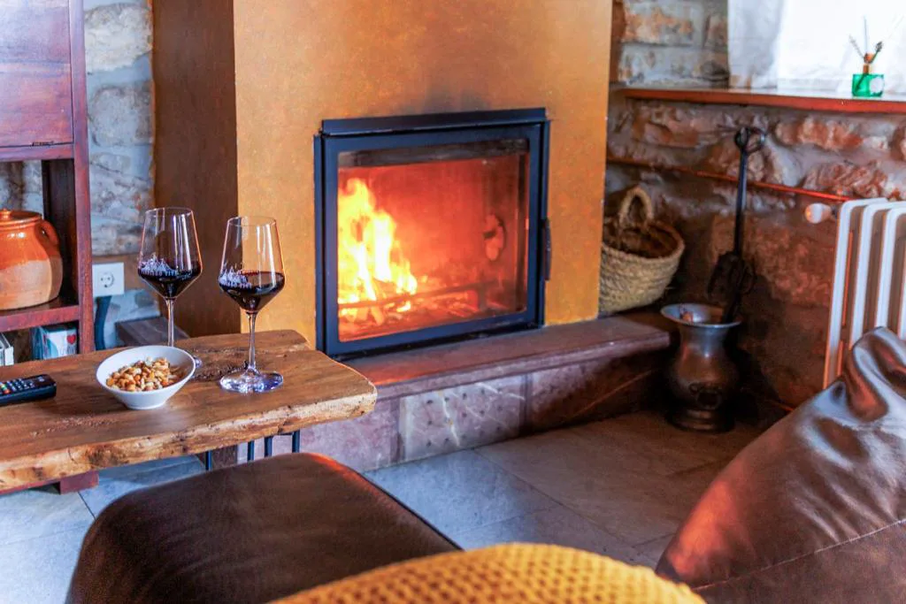 Chimenea encendida junto a un sillón y dos copas de vino