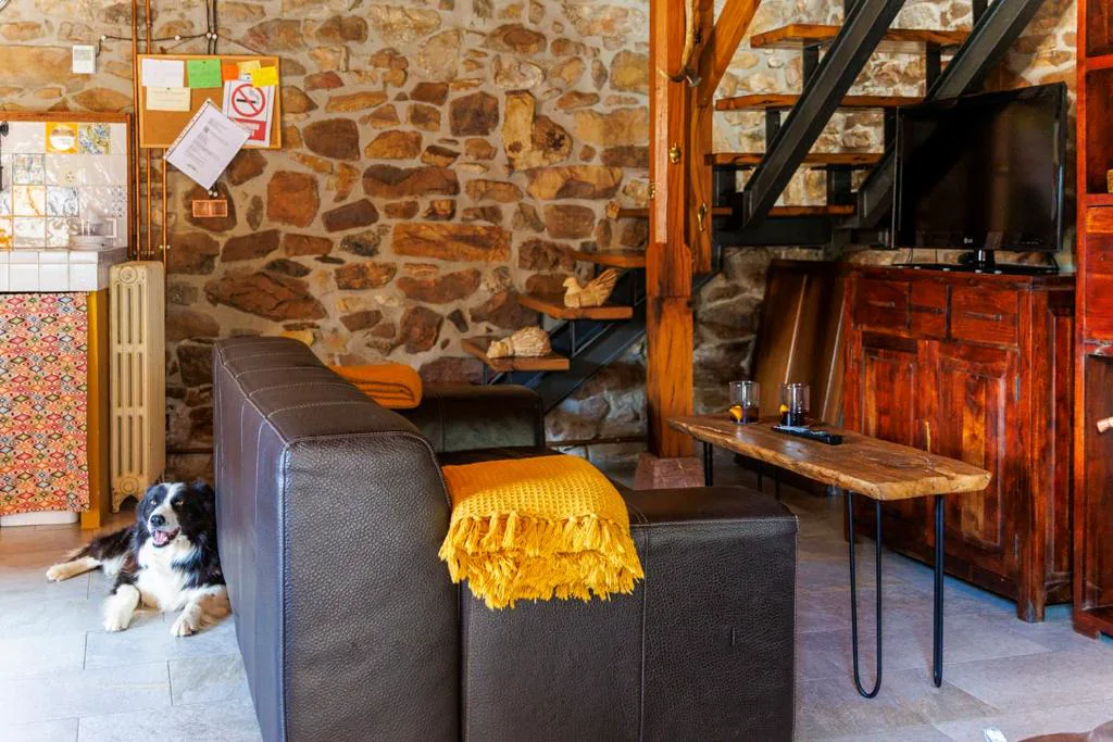 Salón de piedra con sofá negro, escalera y televisor