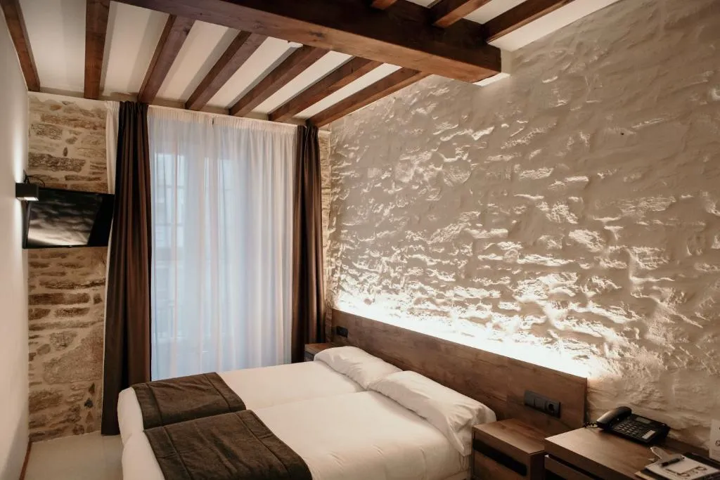 Dormitorio con pared de piedra original iluminada y ropa de cama en tonos neutros, Via Aetcal Hotel & Wellness