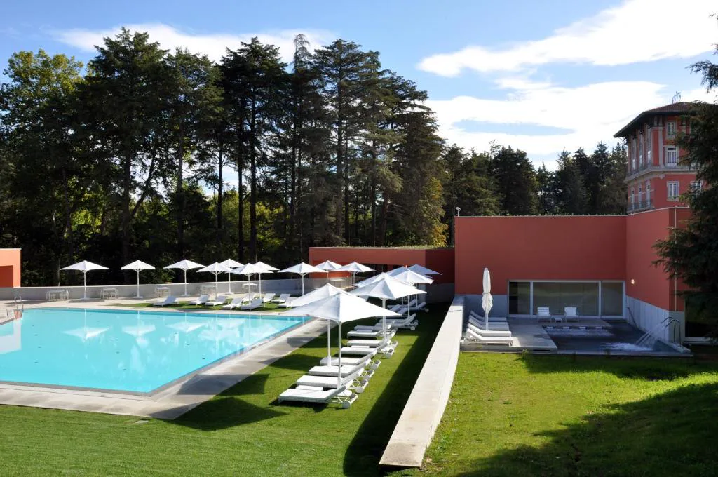 Piscina exterior con tumbonas junto al edificio del spa, entre árboles del parque termal