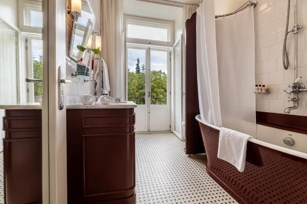 Baño vintage con bañera exenta en tonos burdeos y acceso a balcón, Vidago Palace