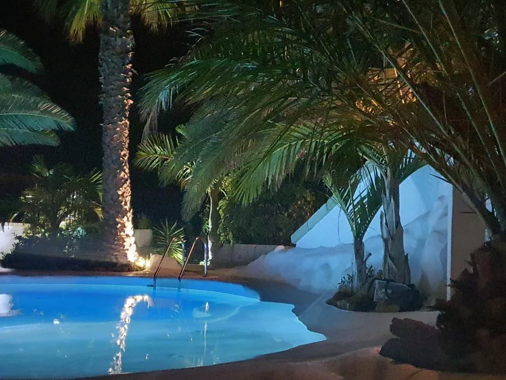 Piscina privada iluminada de noche entre palmeras, Villa Adriano