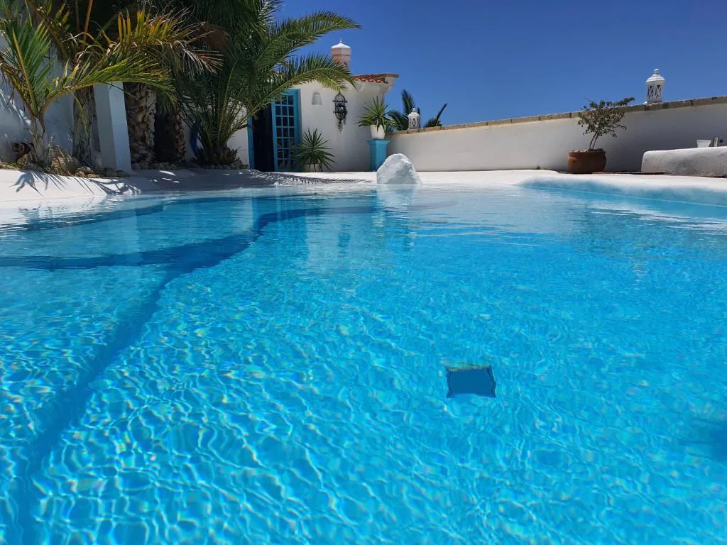 Piscina de agua turquesa junto a la fachada blanca con puerta azul canaria, Villa Adriano