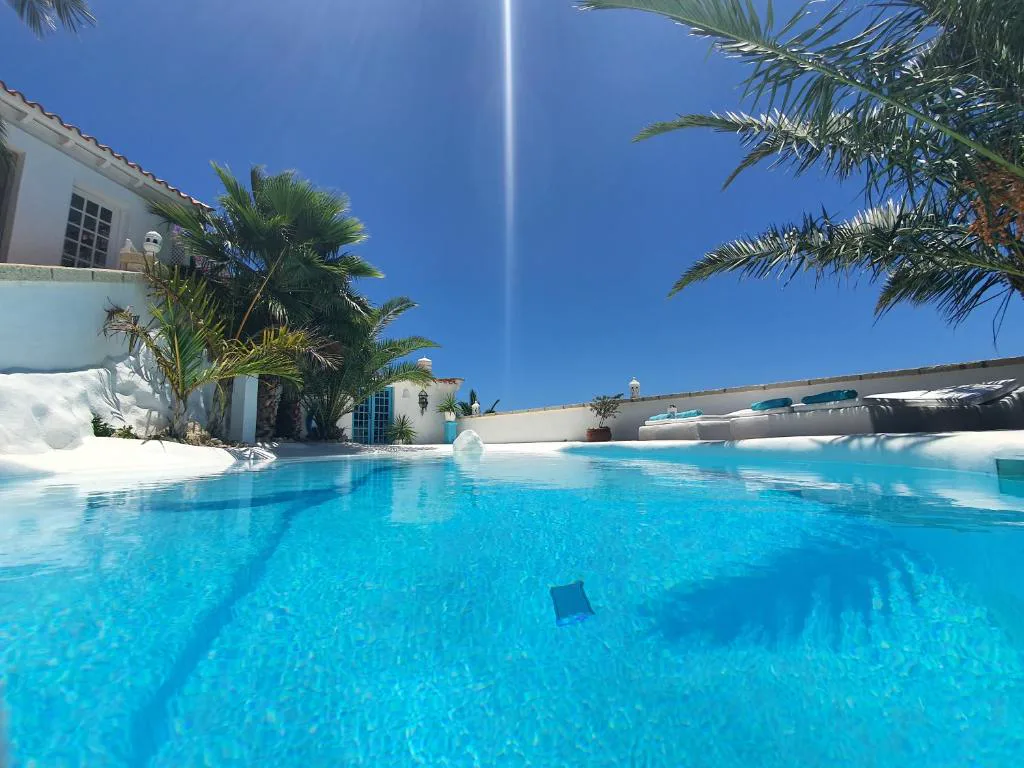 Vista de la piscina con la villa blanca y palmeras al fondo, Villa Adriano