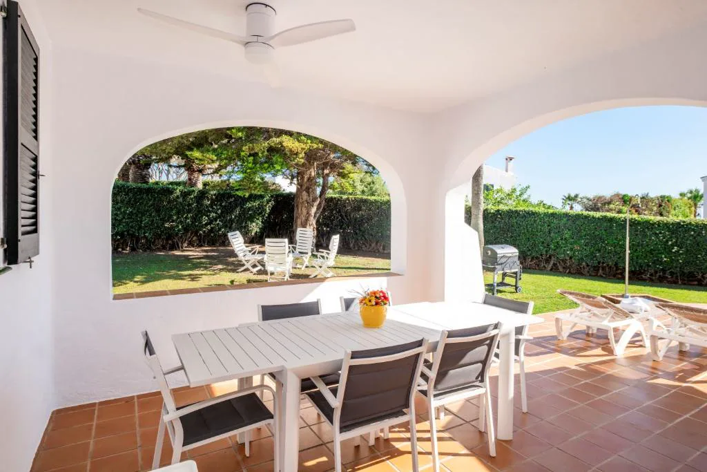 Terraza cubierta con mesa puesta y vistas al jardín arbolado, Villa Binigo