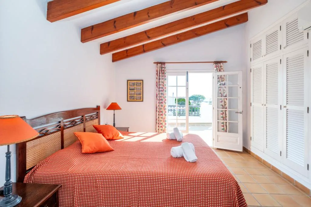 Dormitorio con cabecero de madera tallada y ropa de cama en tonos naranjas, Villa Binigo