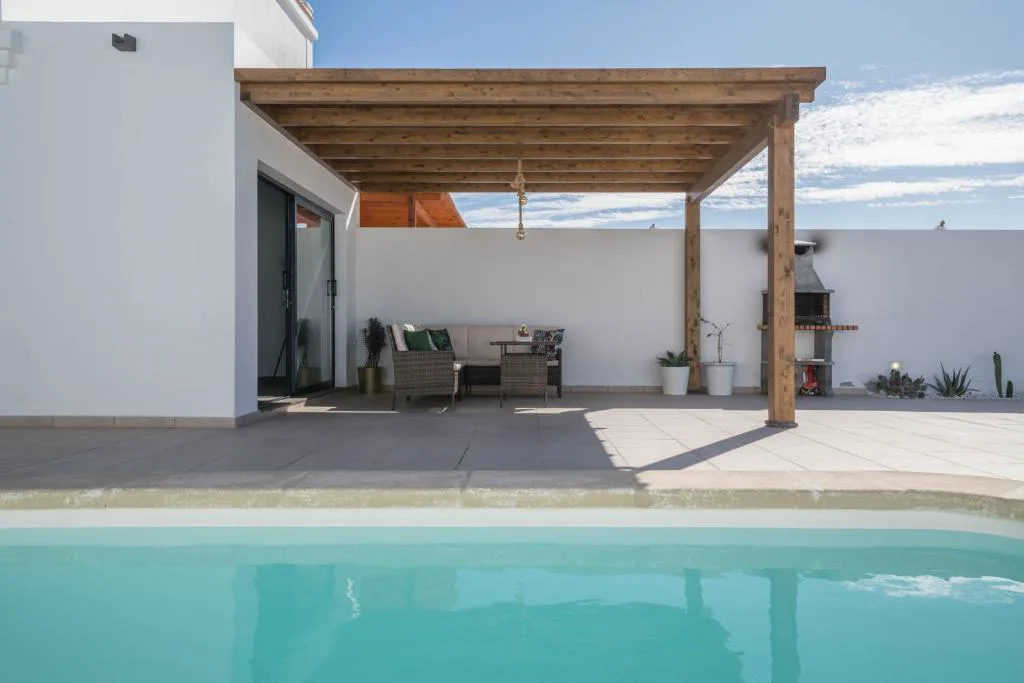 Pérgola de madera con sofá de exterior y barbacoa de obra junto a la piscina, Villa Esmeralda