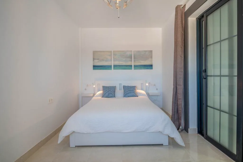 Dormitorio blanco con cuadros marinos y balcón acristalado, Villa Esmeralda