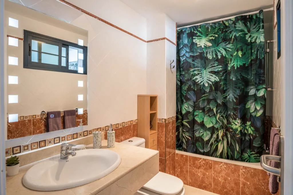 Baño con cortina de ducha de estampado tropical y azulejos color terracota, Villa Esmeralda