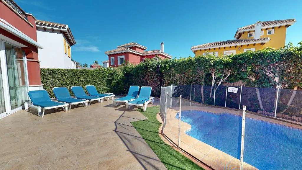 Piscina privada con tumbonas azules junto a una villa roja
