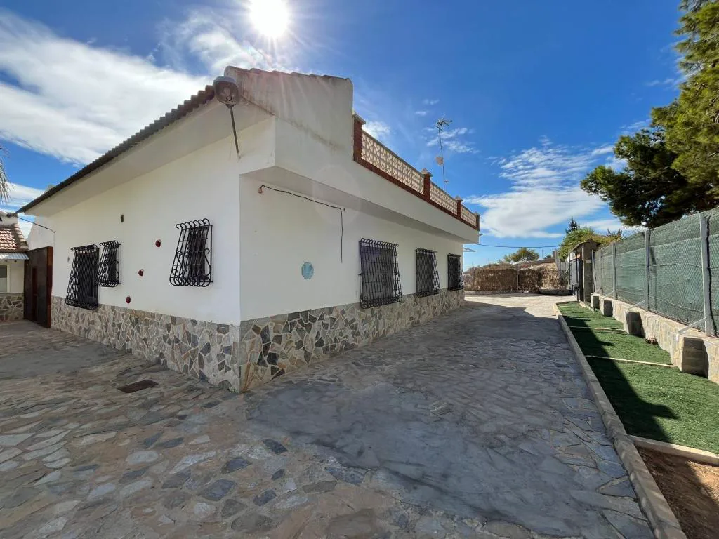 Fachada blanca de la villa con muro de piedra
