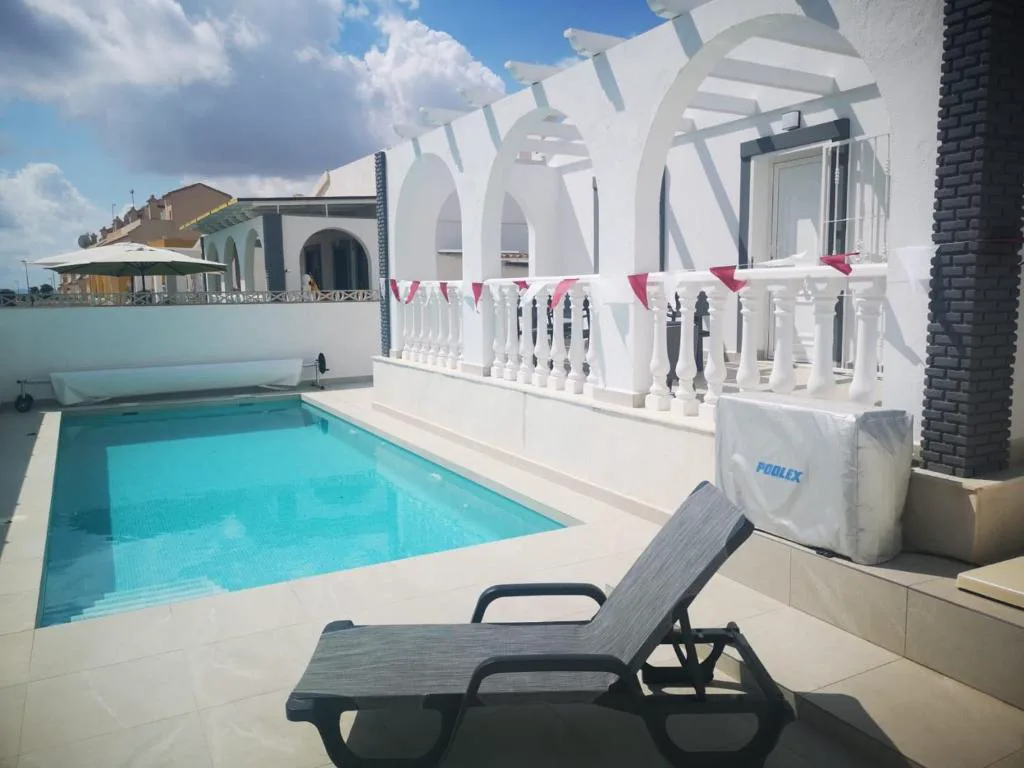 Piscina turquesa junto a una terraza con tumbona