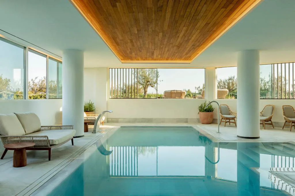 Piscina interior climatizada con columnas blancas y techo de madera, Villa Le Blanc