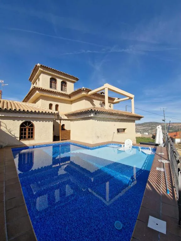Piscina azul en un patio con palmeras y una casa con balcón