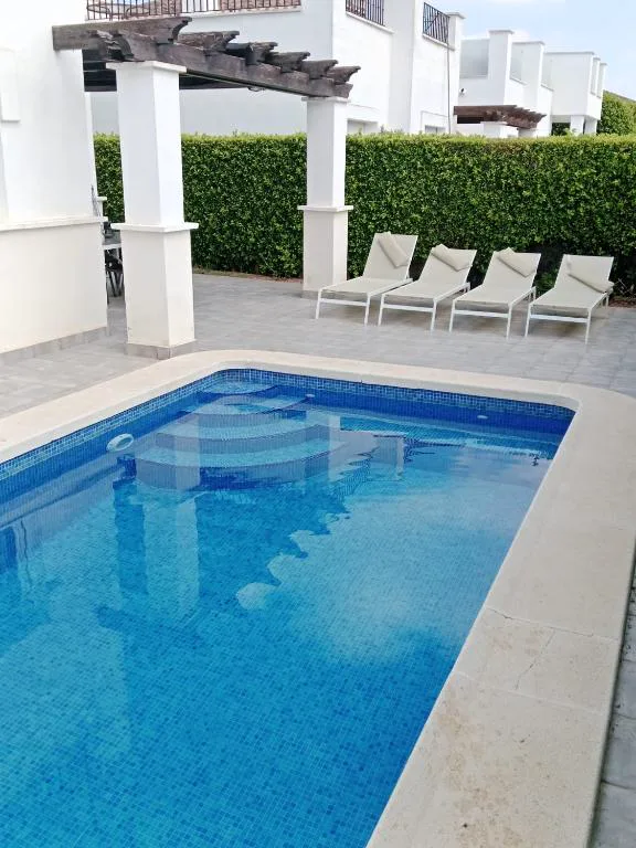 Piscina azul con tumbonas blancas junto a la casa