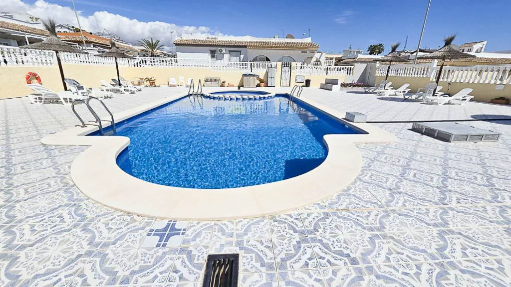 Piscina comunitaria con azulejos y tumbonas bajo el sol