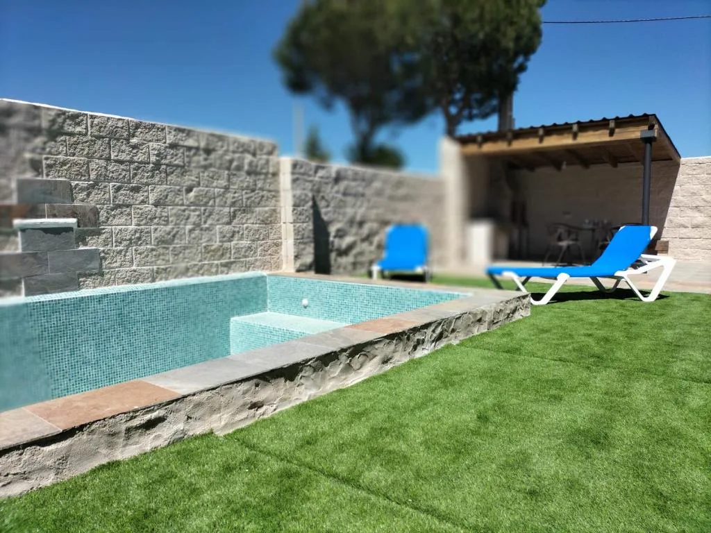 Piscina privada con tumbonas azules, césped y pared de piedra