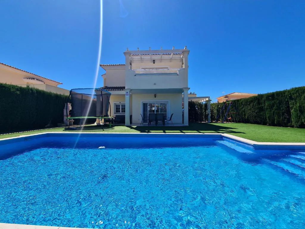 Piscina privada azul con césped artificial y una casa blanca