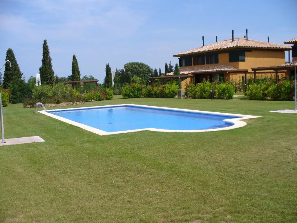 Piscina comunitaria entre césped y villas de estilo mediterráneo