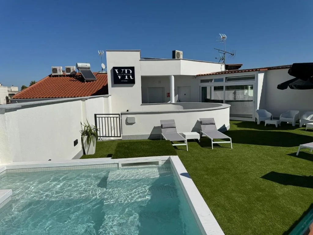 Piscina rodeada de césped artificial junto a una terraza blanca
