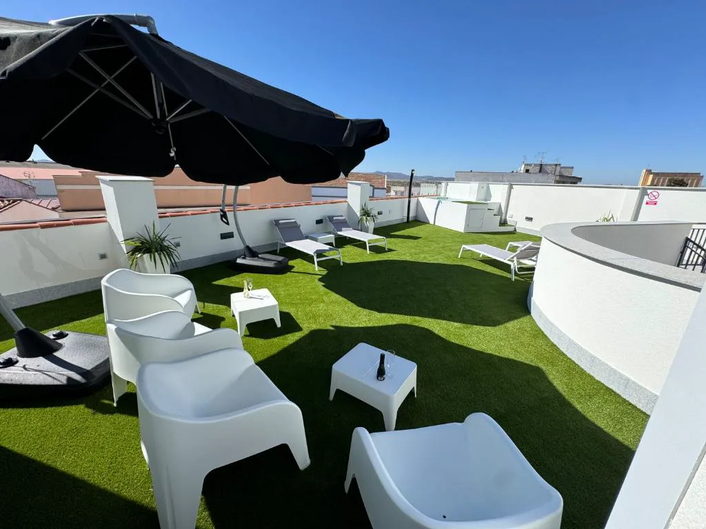 Terraza con césped artificial, sombrilla y sillones blancos