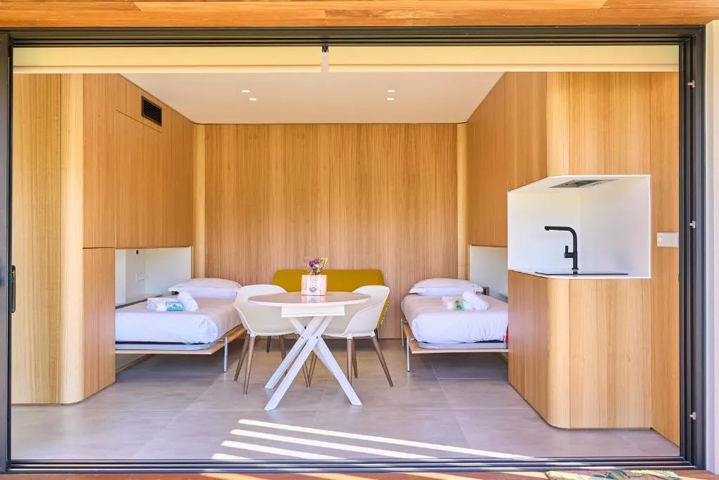 Salón con dos camas individuales, mesa y cocina compacta integrada en madera