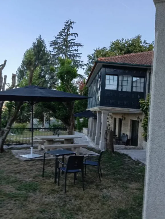 Terraza ajardinada con mesa, sillas y sombrilla frente a la galería acristalada, Hotel Rural VN Tenorio
