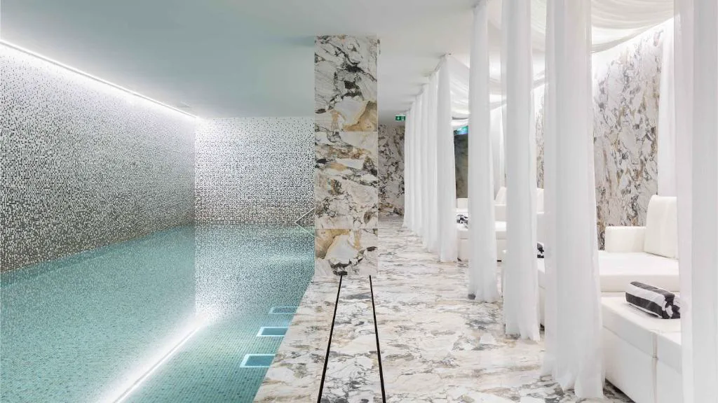 Piscina interior de mosaico de mármol de Wine & Books Porto Hotel, flanqueada por cortinas blancas translúcidas